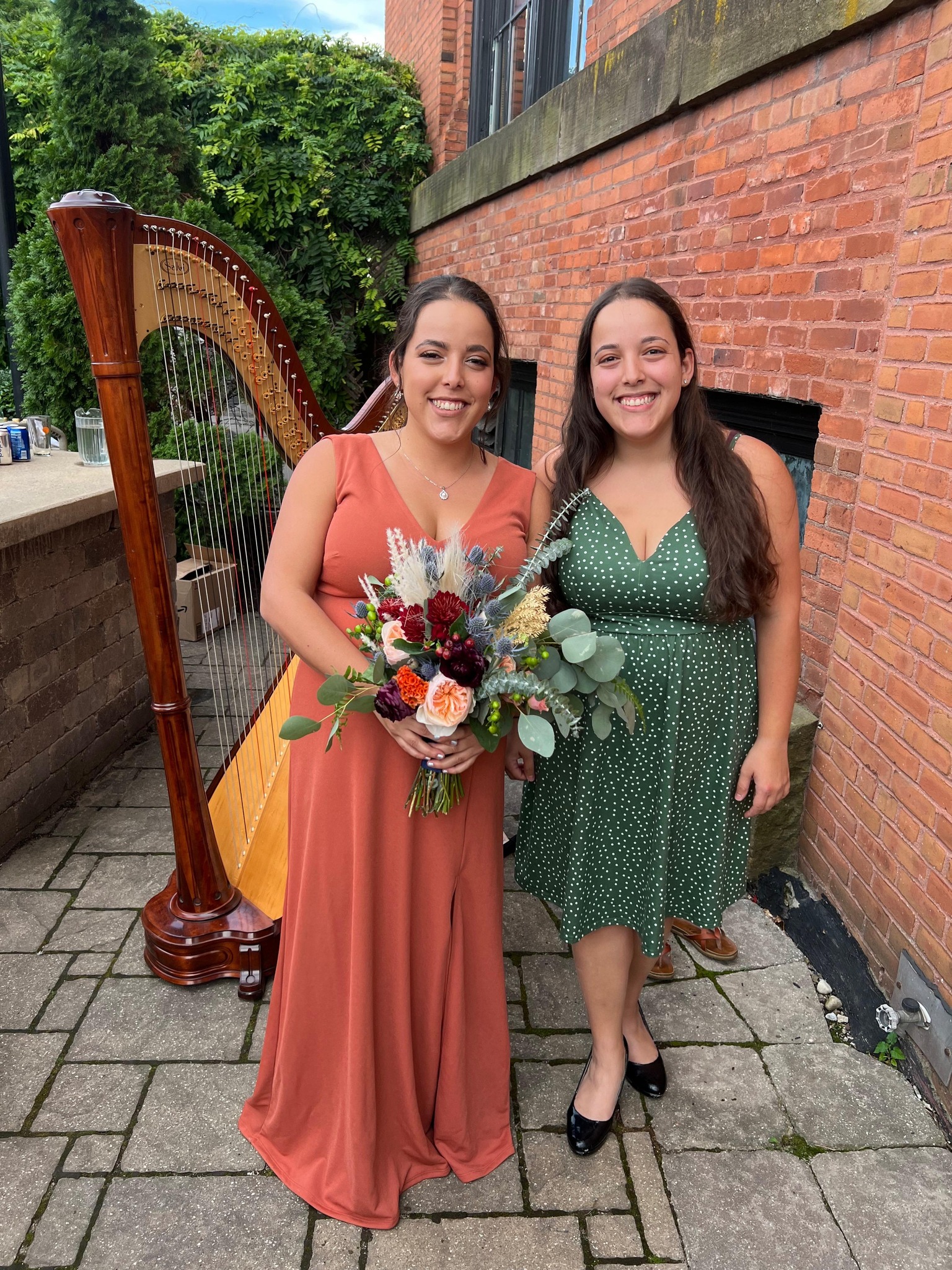 Book a Harpist for your Wedding. Maia posing with bridesmaid with her harp in the background.  